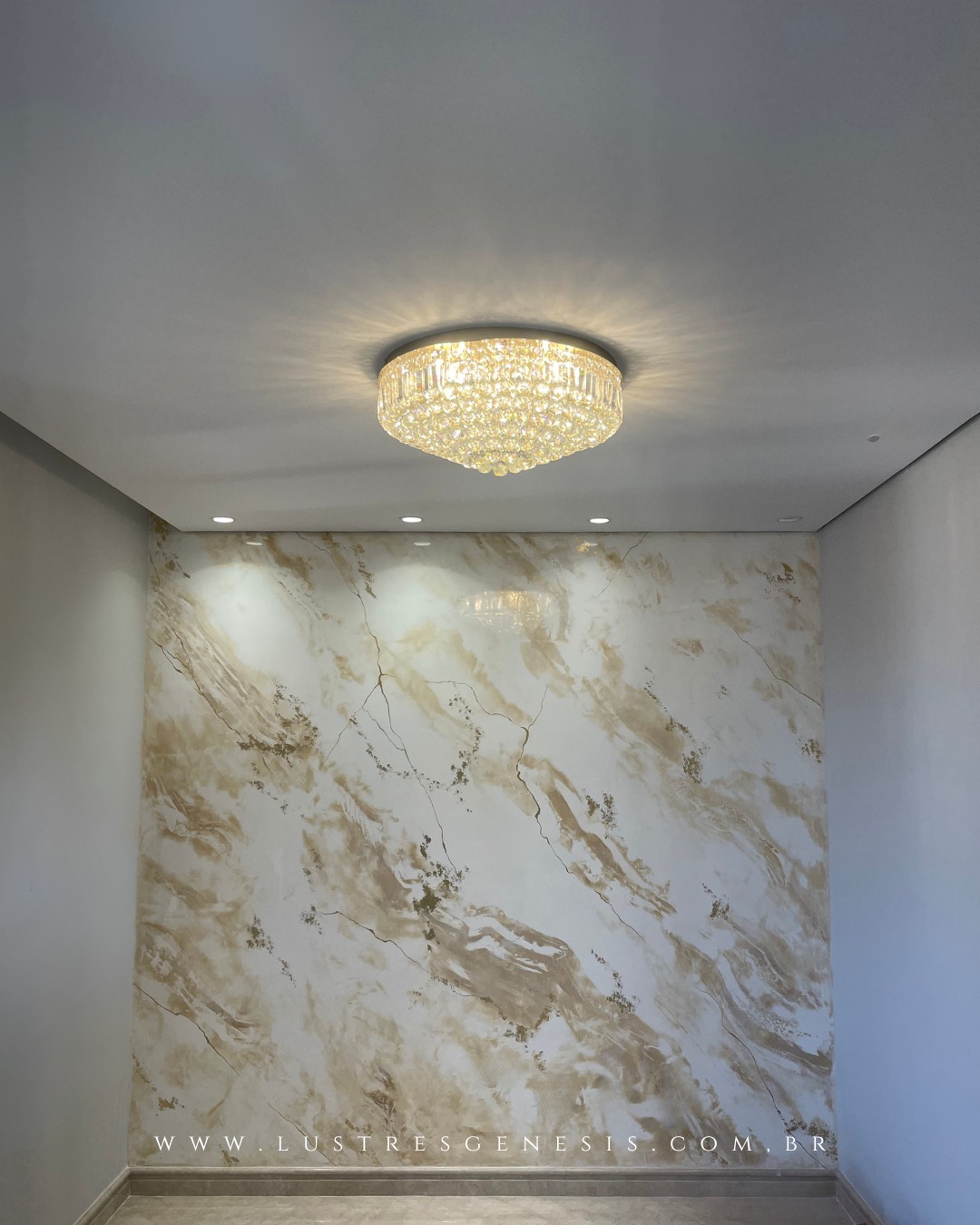 Lustre de cristal redondo Harion Ø50 Dourado com pedras transparente da Lustres Gênesis instalado no teto, iluminando ambiente sofisticado com parede marmorizada.